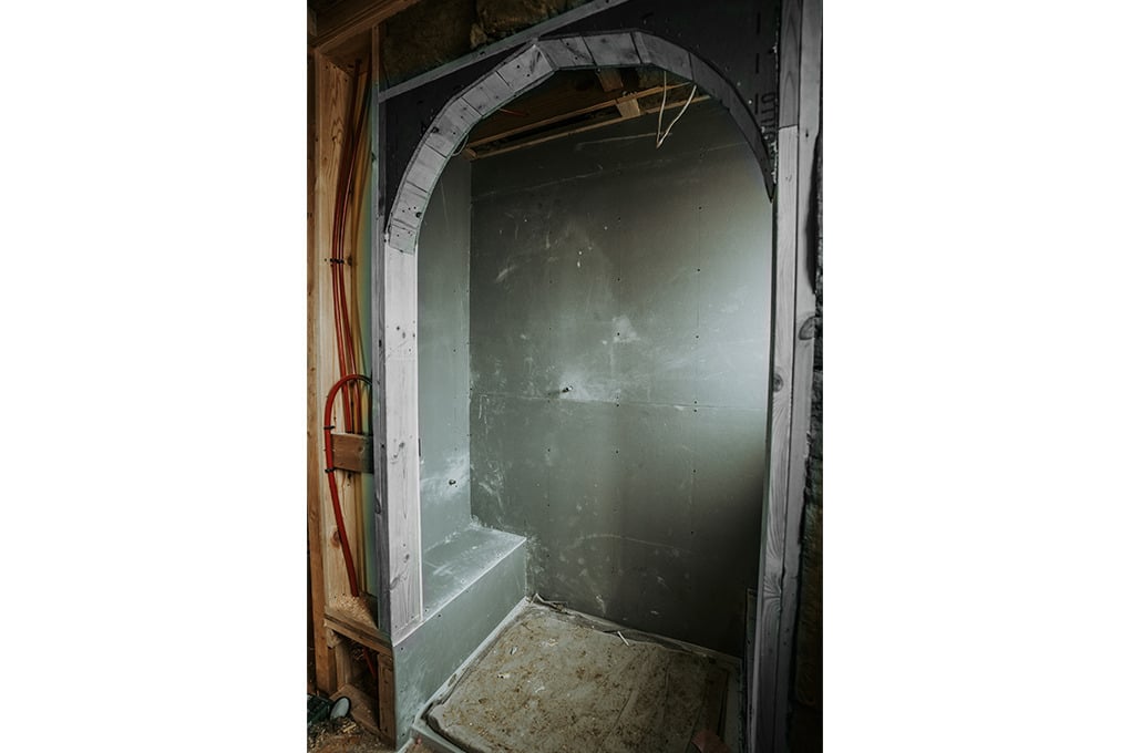 Framed shower space under construction featuring grey moisture-resistant wall panels on three sides, a built-in bench on the left, an arched wall opening with exposed framing, and a rough floor base.