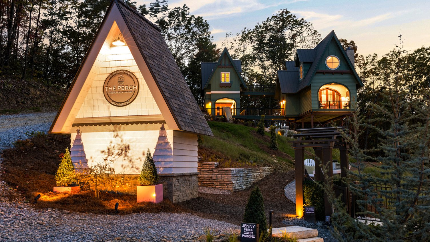 Modern elevated treehouse-style home at The Perch at Pinhoti Peak, featuring dark exterior cladding, expansive windows, and a wraparound deck overlooking a wooded mountain landscape.