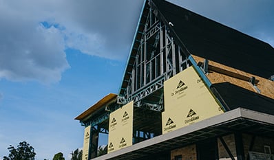 Modern elevated treehouse-style home at The Perch at Pinhoti Peak, featuring dark exterior cladding, expansive windows, and a wraparound deck overlooking a wooded mountain landscape.
