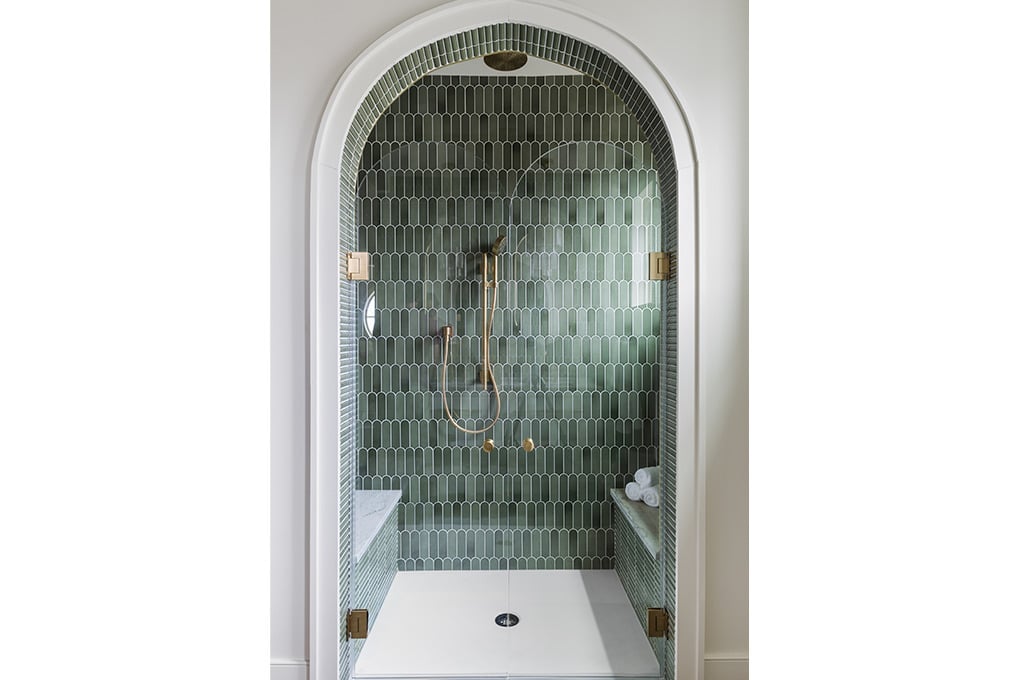 Well-designed interior corner of a Perch at Pinhoti Peak treehouse featuring an arched opening painted a contrasting color leading into a relaxed seating area with a curved upholstered chair, built-in bench with cushions and books, floral wallpaper and a pendant light, all atop wood-tone flooring.