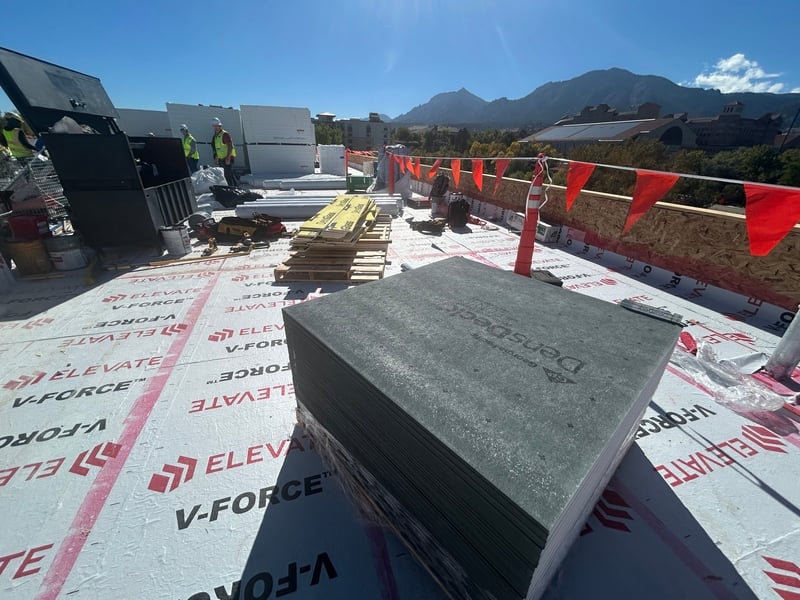 Roofing professionals from JR & Co. working on a commercial roofing project, installing materials on a flat roof under clear skies.