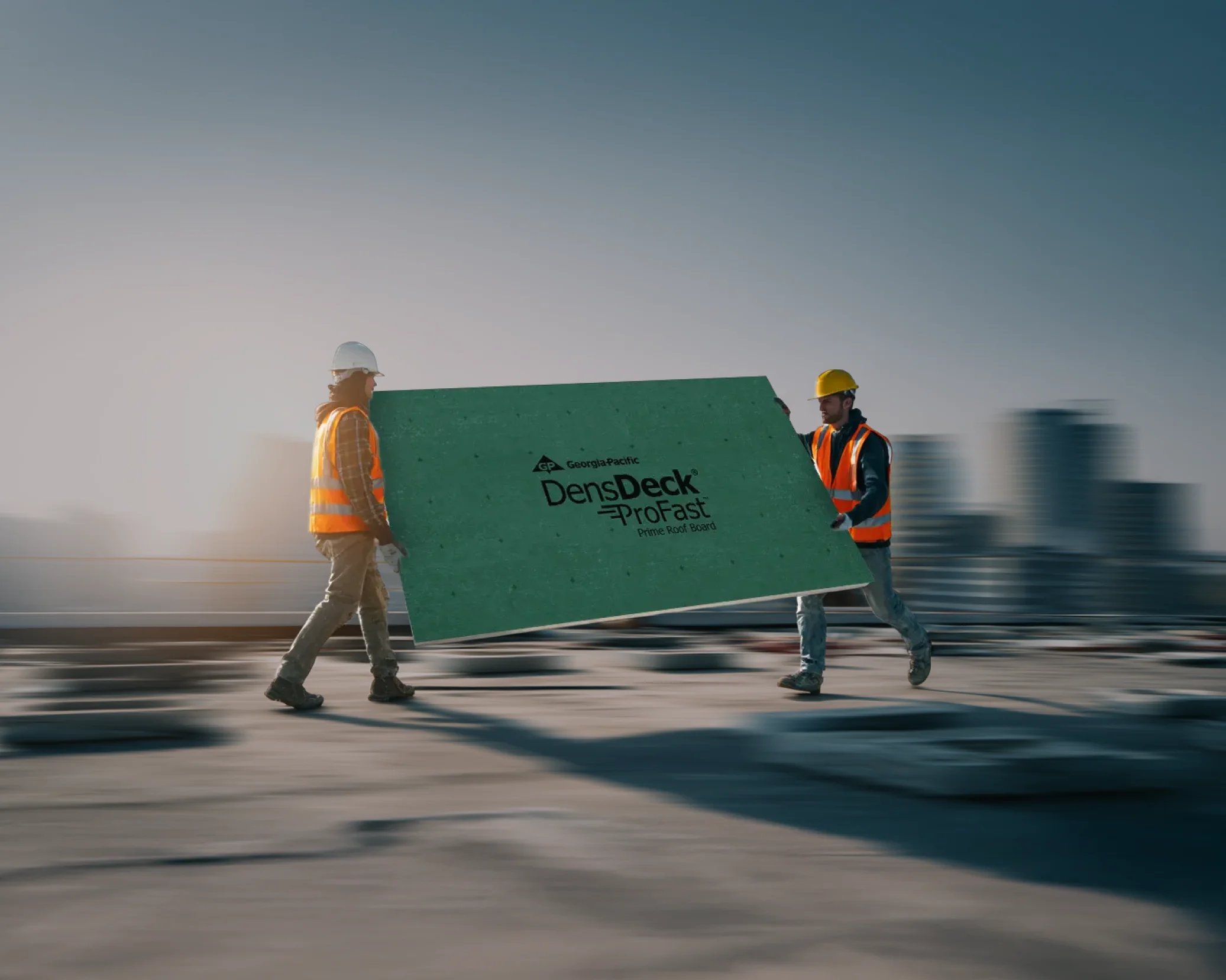 Two men in hard hats and orange vests carry a green DensDeck® ProFast™ Prime Roof Board between them on a rooftop.